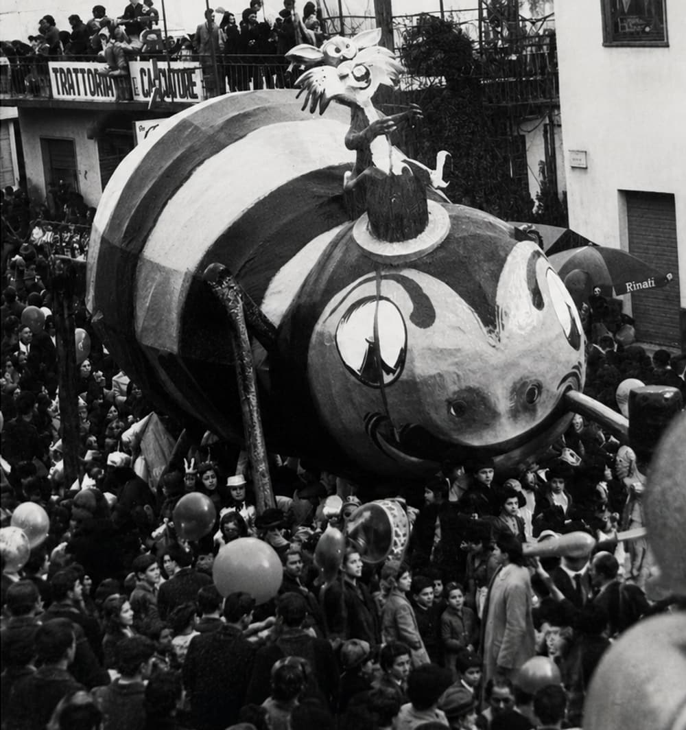 A giant papier-mâché float towers over the crowd in the village street in a black-and-white photograph from the early Carnevale years