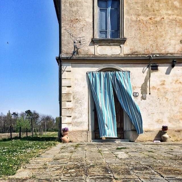 A farmhouse doorway at corte Brogi with a striped curtain, stone paving in front and fields behind