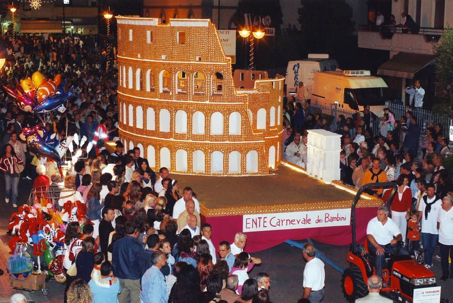 The Dolcione as a giant Colosseum in pastry, paraded through a night-time crowd in Orentano